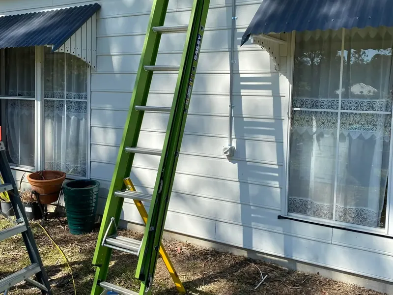 A ladder set against the weatherboard wall of a coastal home during a service call