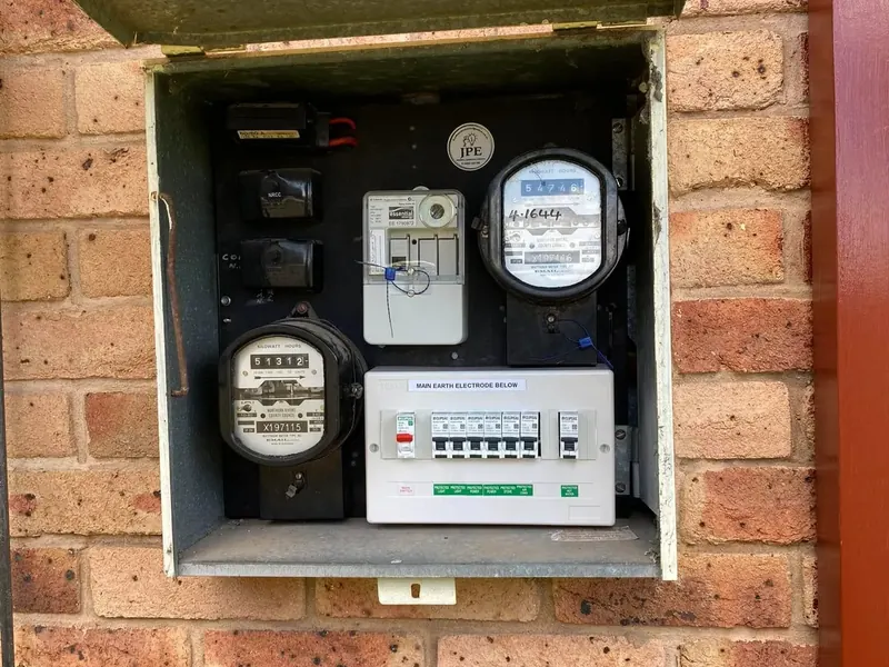 An opened meter box showing older meters beside a newer circuit breaker board
