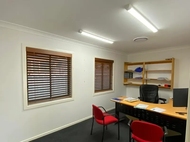 A small office lit by a ceiling batten light above a desk and chairs