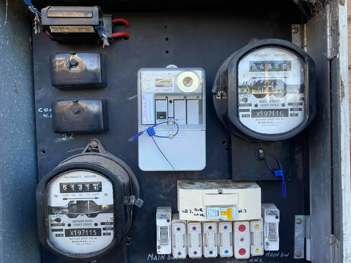 An older meter box opened up showing ageing meters, fuses and the main switch